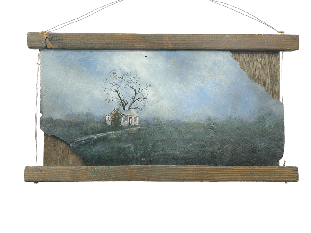 A rustic acrylic painting on a weathered slate shingle depicts a small, aged cabin in a misty rural landscape. A leafless tree stands behind the cabin, silhouetted against an overcast sky. The scene evokes a somber, quiet mood. The painting is framed in rough-hewn wood, enhancing its natural and reclaimed aesthetic.