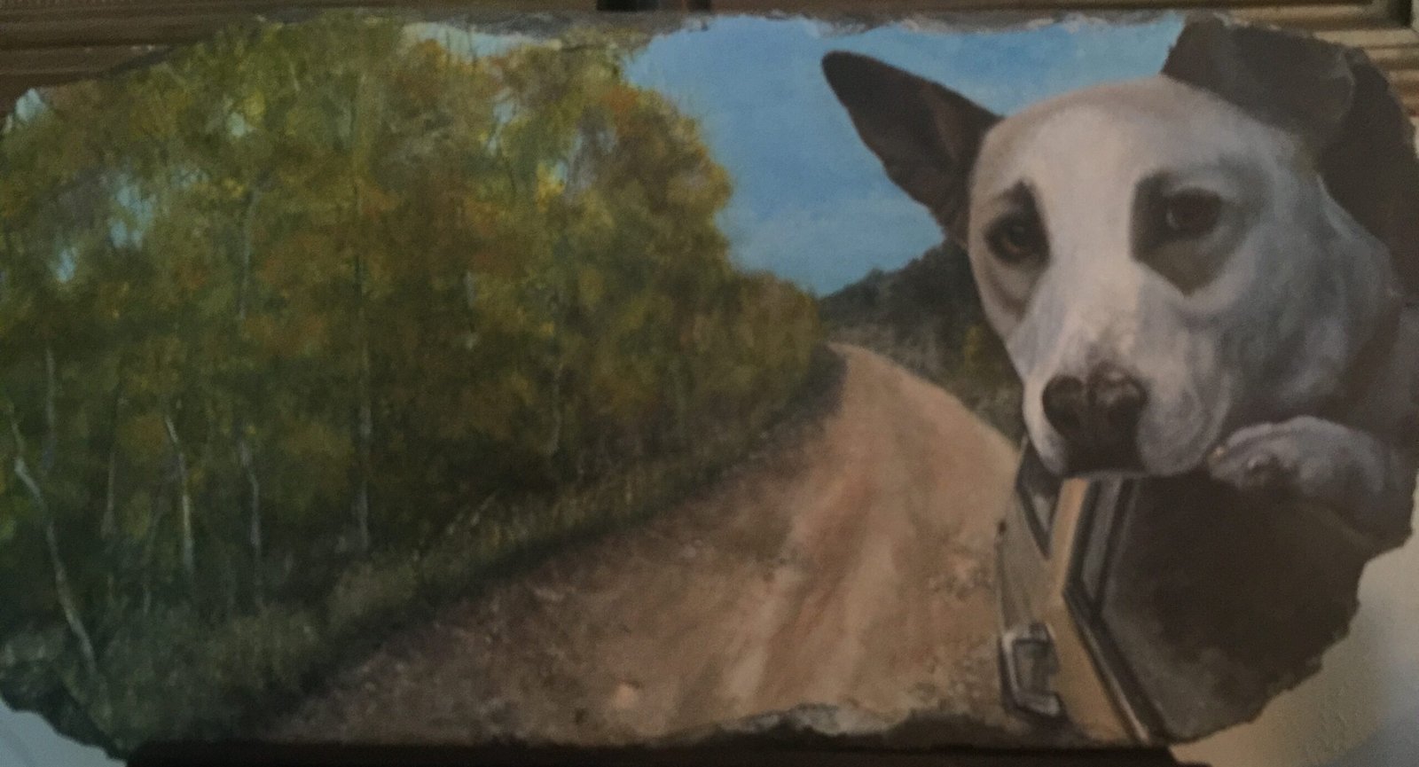 Portrait of a white dog leaning out of a car window, painted on a weathered slate shingle. The dog’s gaze meets the viewer with quiet joy as the car winds down a forested dirt road under a clear blue sky. Autumn foliage glows along the roadside, echoing the warmth of the moment. The aged slate carries the texture of time, grounding the scene in memory, movement, and companionship.