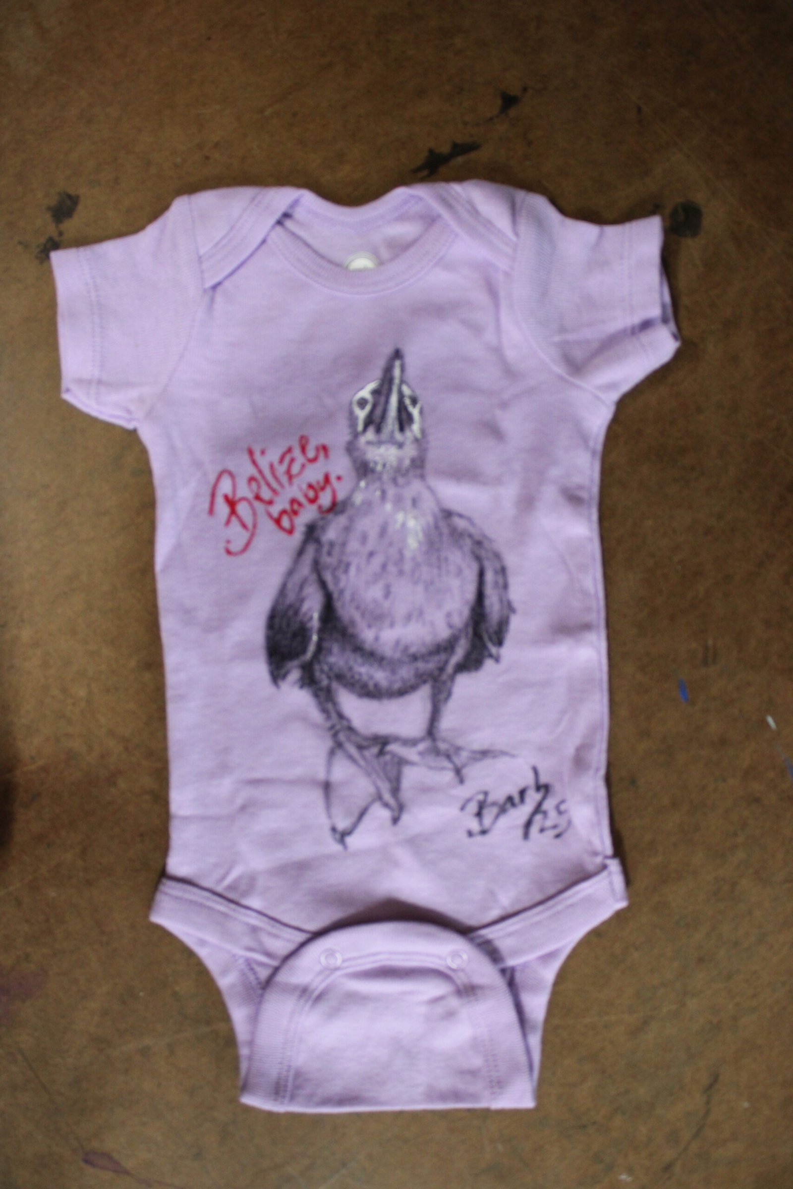 Light purple baby onesie featuring a bold pigeon and the phrase “Belize, Baby!”—a cheeky nod to the tropical rendezvous in Belize that led to this tiny human’s grand debut. Equal parts souvenir and sass, it’s wearable proof that birds aren’t the only ones nesting.