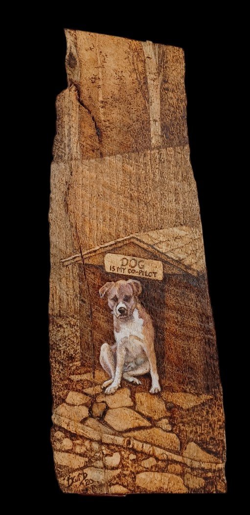 Wood burning portrait of Artie, a small dog seated peacefully on a stone path before a rustic wooden door. Above him, a sign reads “DOG is my copilot,” transforming the scene into a quiet tribute. Rich textures in the wood grain, stonework, and Artie’s fur evoke warmth and companionship. Commissioned to honor Artie’s loyal presence and the soulful bond between human and dog.